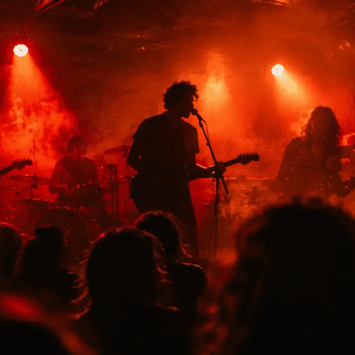 Maré Vermelha se apresentando ao vivo em palco pequeno, com luzes vermelhas e silhuetas da banda em contraluz